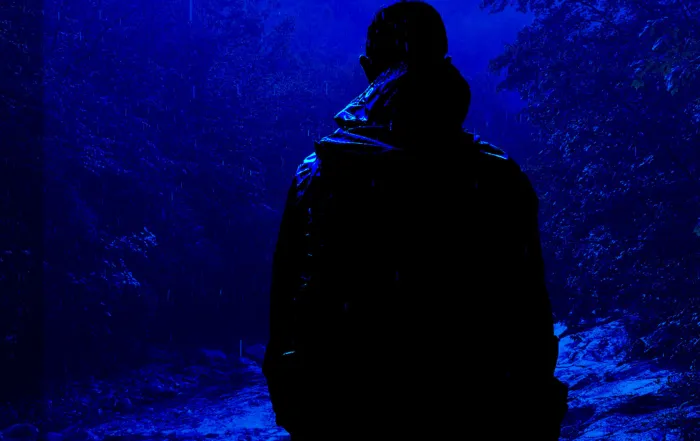 Silhouetted hiker standing alone in a dark, rainy mountain forest at night, overlooking a rushing creek. Atmospheric blue cover for the short story "The Life and Death of an Unimportant Man" by Zac Northup.
