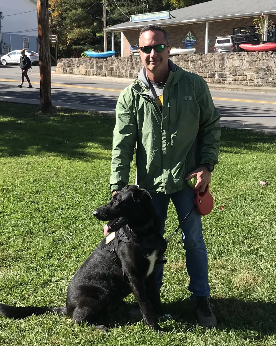 Zac Northup in a green jacket with his black dog.